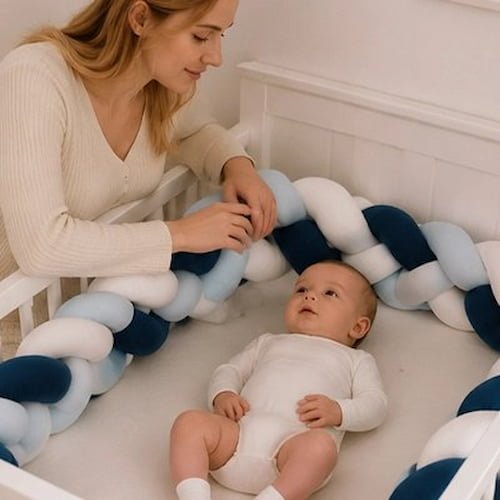 Bébé repose dans son berceau entouré d’une tresse de lit bleu, blanc et gris