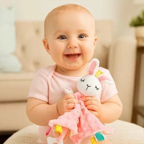 bebe souriant tenant un doudou lapin rose avec un corps de couverture rose pointille
