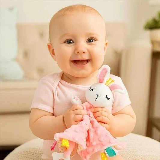 bebe souriant tenant un doudou lapin rose avec un corps de couverture rose pointille