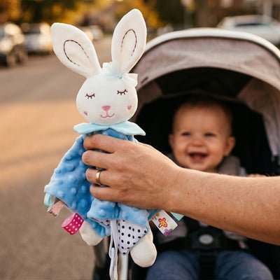 lapin doudou bleu en tissu minky tenu devant une poussette avec un bébé souriant dehors