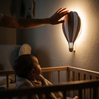 Bébé observe la douce lumière d'une veilleuse murale bebe en forme de montgolfière