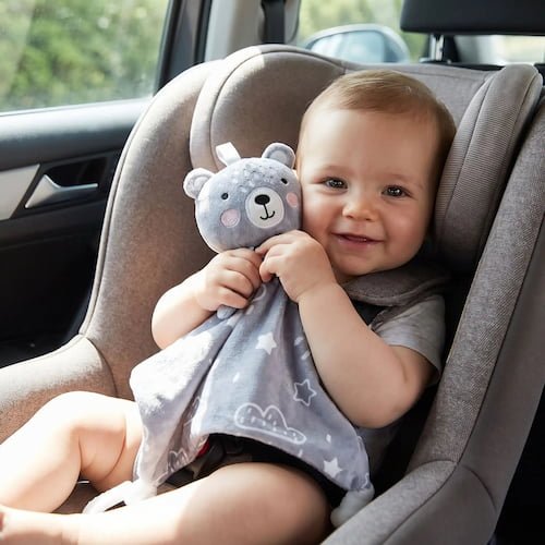 bebe souriant dans un siege auto tenant un doudou bebe garcon ours gris pour un trajet confortable