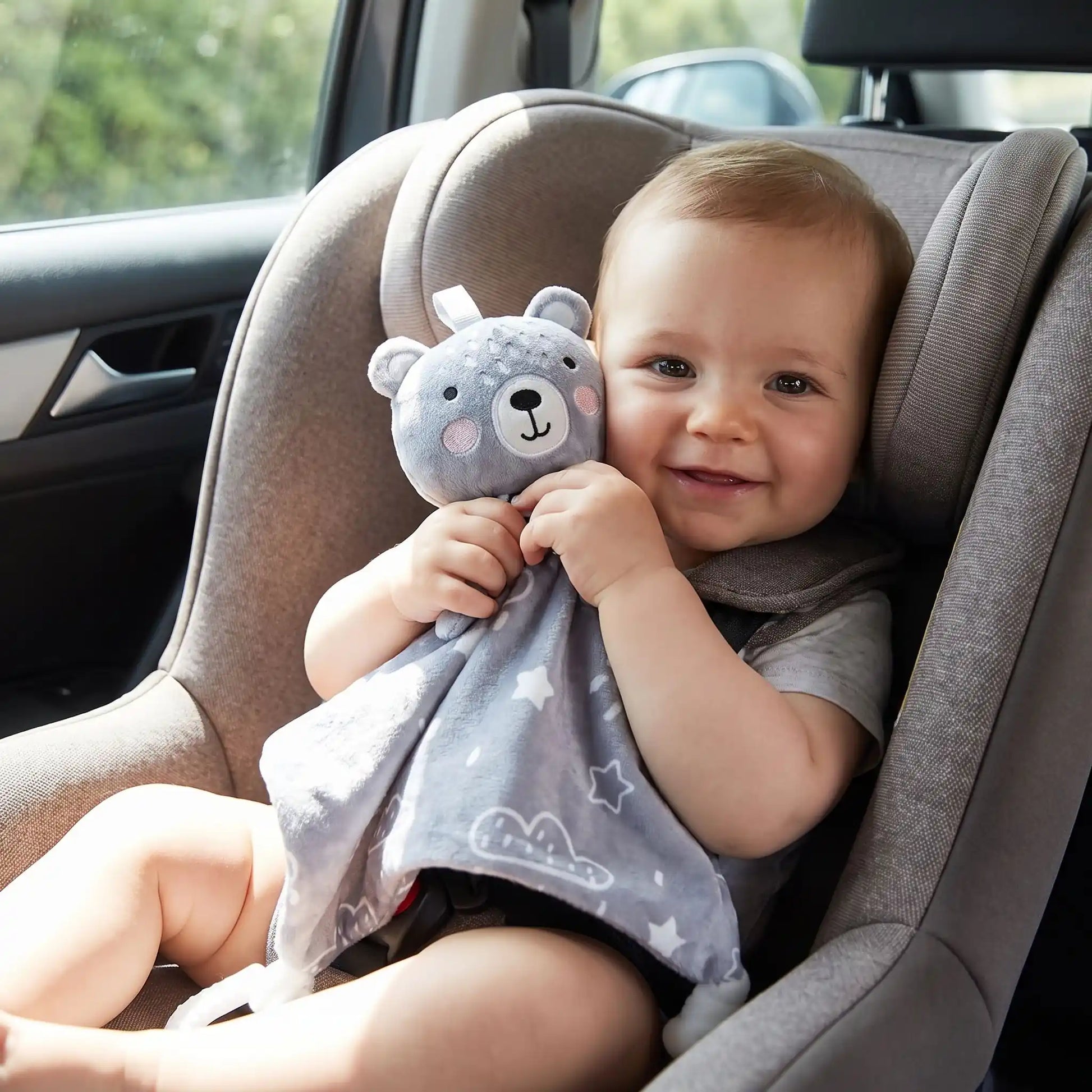 bebe souriant installe dans un siege auto tenant un doudou ours gris ultra doux avec anneau de dentition pour un trajet confortable