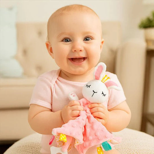 bebe souriant tenant un doudou lapin rose avec un corps de couverture rose pointille