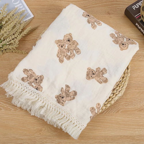 Couverture bébé beige à motifs ours et franges  pliée et présentée sur un panier