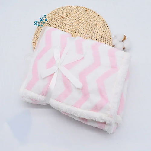 Couverture bébé rose et blanche à motifs chevrons pliée avec nœud
