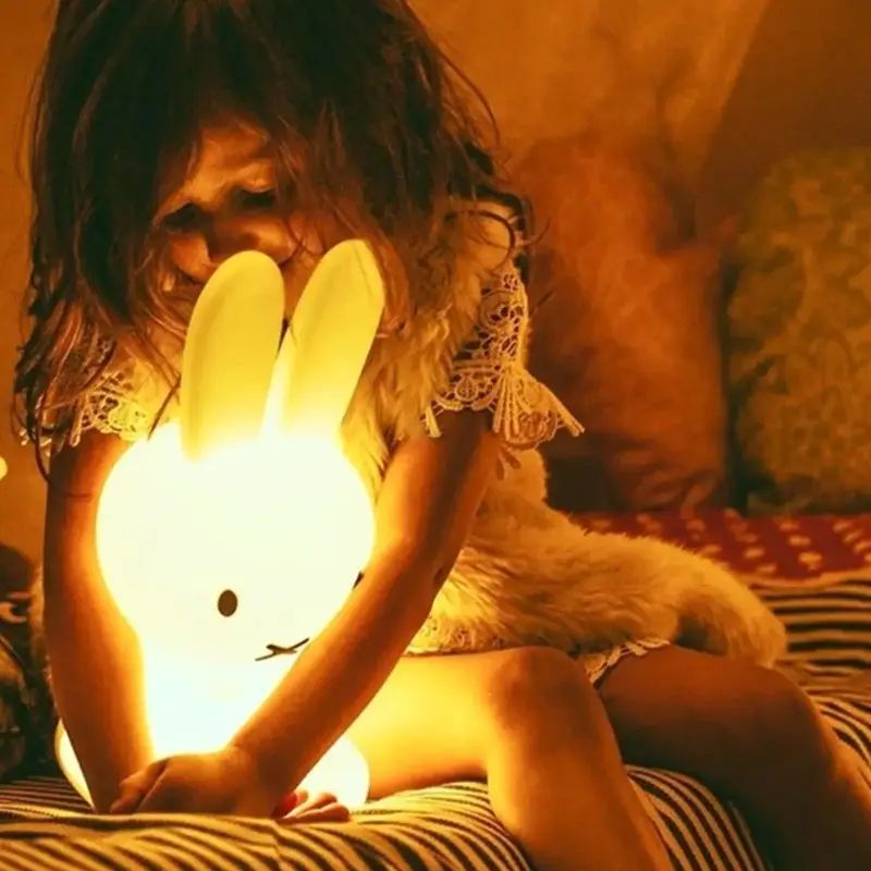 Enfant câlinant une veilleuse lapin allumée dans une chambre pour une ambiance réconfortante
