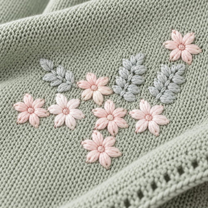 Gros plan sur une couverture tricot pour bebe verte avec de jolies fleurs roses et un feuillage délicat brodé
