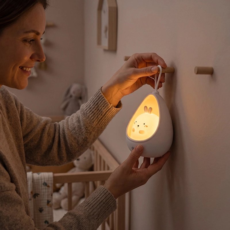 Maman installe une veilleuse pour bébé au mur près du lit de son bébé