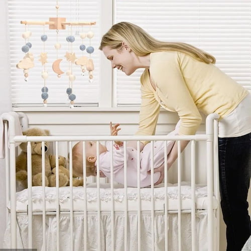 Maman presente un mobile bebe avec etoiles lunes et nuages au dessus du lit de bebe
