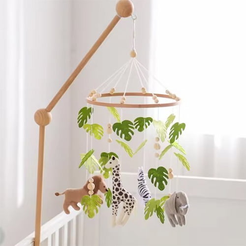 Mobile bébé motif safari installé au-dessus du berceau avec des animaux et des feuilles tropicales