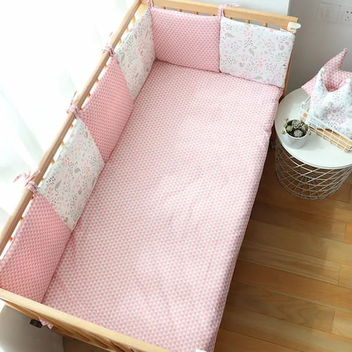 Tour de lit bebe rose à motifs cygles et fleurs installé autour d’un lit en bois
