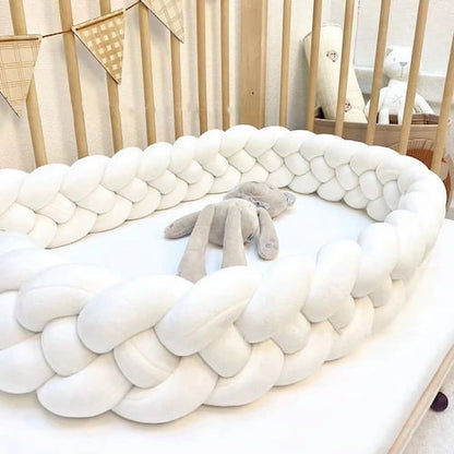 Tour de lit tressée blanche disposée autour d’un lit bébé en bois