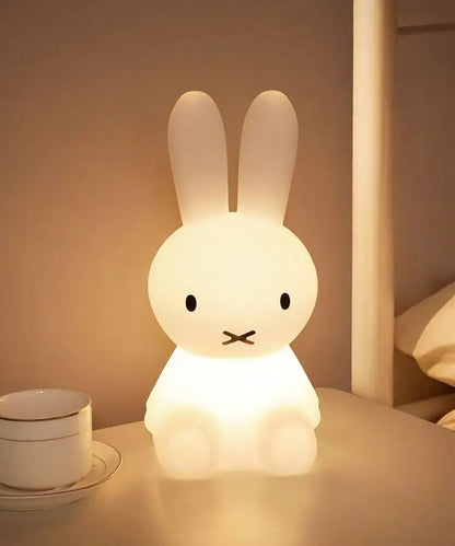 Veilleuse lapin blanc chaud diffusant une lumière douce sur une table de chevet dans une chambre d'enfant
